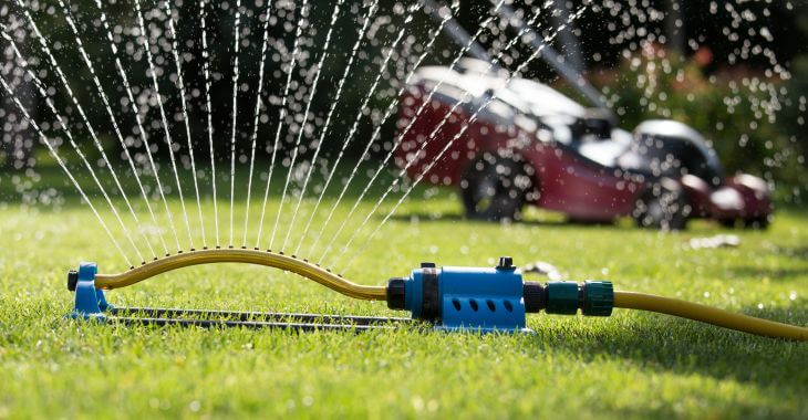 Grass mower and a sprinkler watering grass.