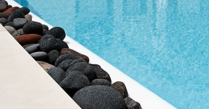 Color lava rocks on the side of the backyard swimming pool.