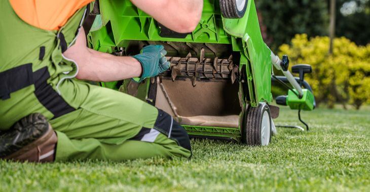 A person checking a dethatcher before lawn thatch removal.