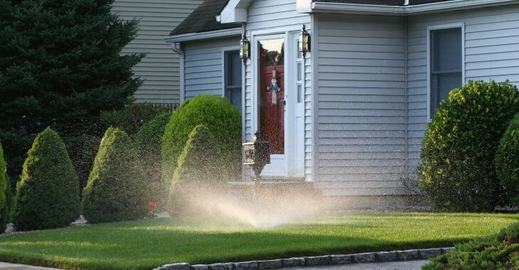 A sprinkler watering lawn and plants in front of a residential house.