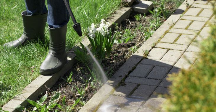 A man power washing concrete paver in his garden.