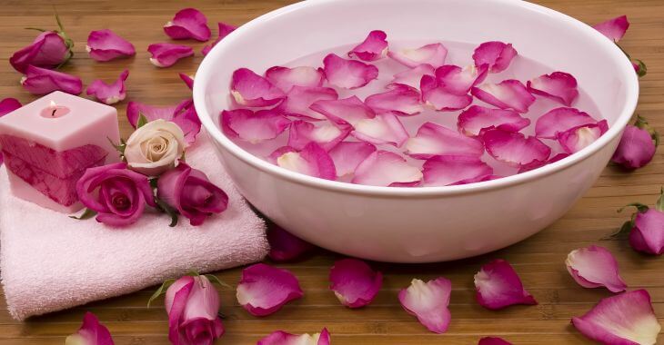 A towel and a pink rose next to a bowl with floating rose petals.