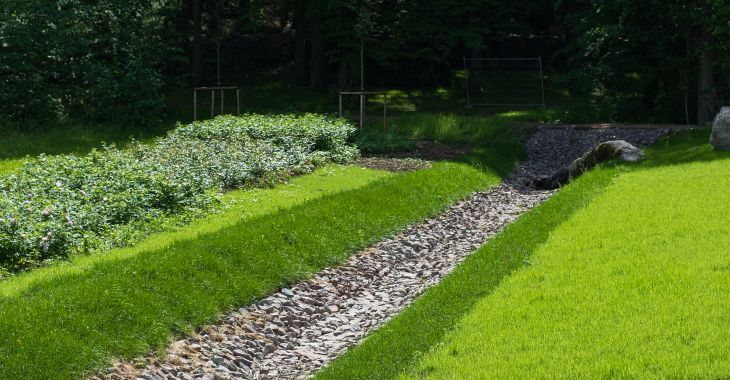 Lawn with a dry creek bed installed as drainage and erosion solution.