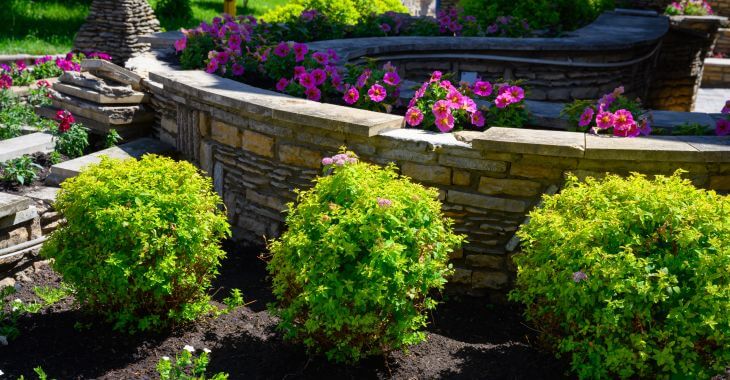 Beautiful garden with retaining decorative wall surrounded by green plants and seasonal flowers.