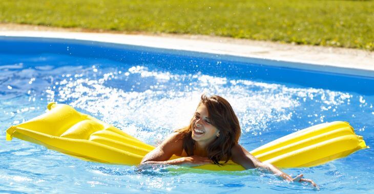 Cheerful young woman with a pool mattress relaxing in the backyard swimming pool.
