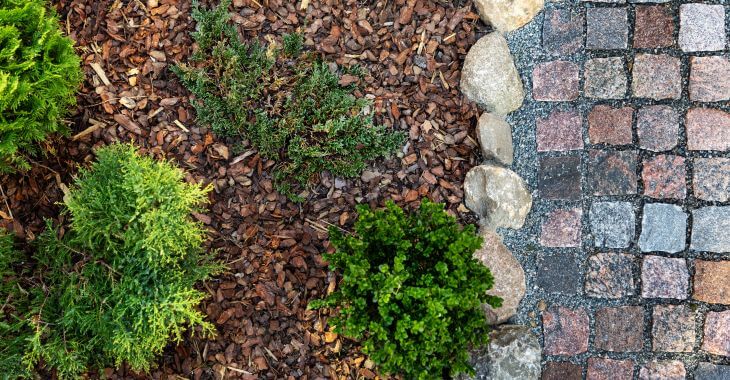 Natural stone paver next to a mulched plant bed with river rock edging