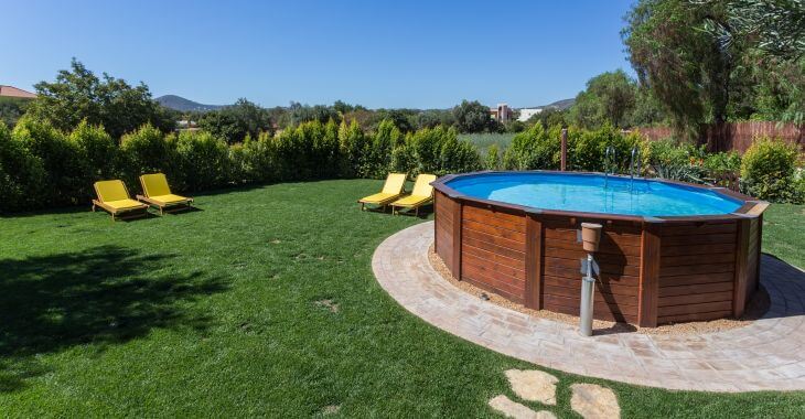 An above-ground pool built on a paver patio in a garden.