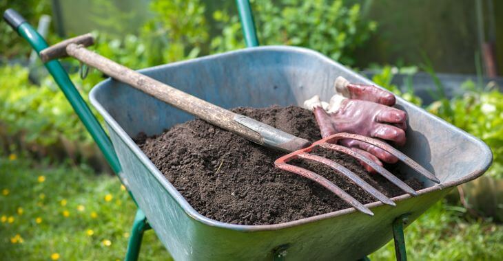 Pitch fork and gardening gloves in wheelbarrow full of humus garden soil
