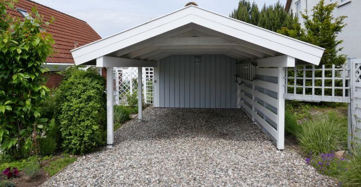 gravel driveway in front of a white wooden carport with pitched roof