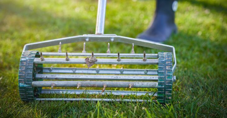 A man using a manual areator to improve lawn quality