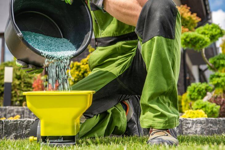 a man pouring lawn fertilizer into the spreader