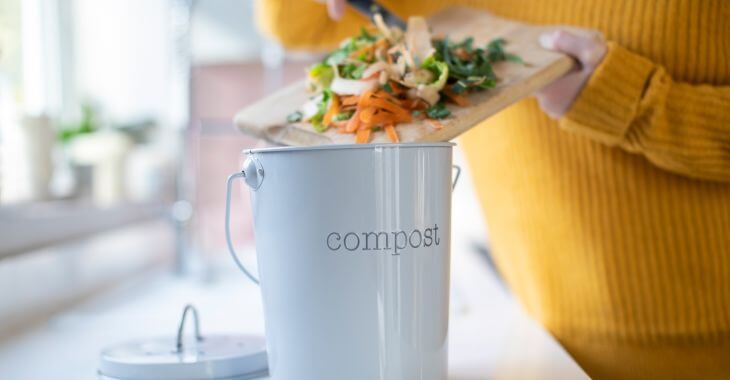 A woman throwing plant food wastes to the kitchen container with sign that reads compost